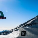 person in green jacket and black pants riding black snowboard on snow covered mountain during daytime