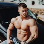 topless man in blue denim jeans sitting on car hood