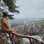 man in brown jacket sitting on tree branch during daytime